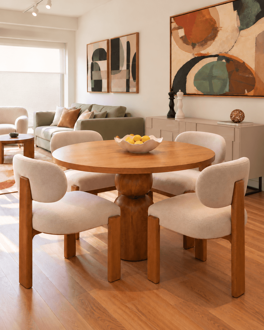 Sala comedor moderna con mesa redonda de madera, cuatro sillas tapizadas y consola decorativa en un espacio social integrado.
